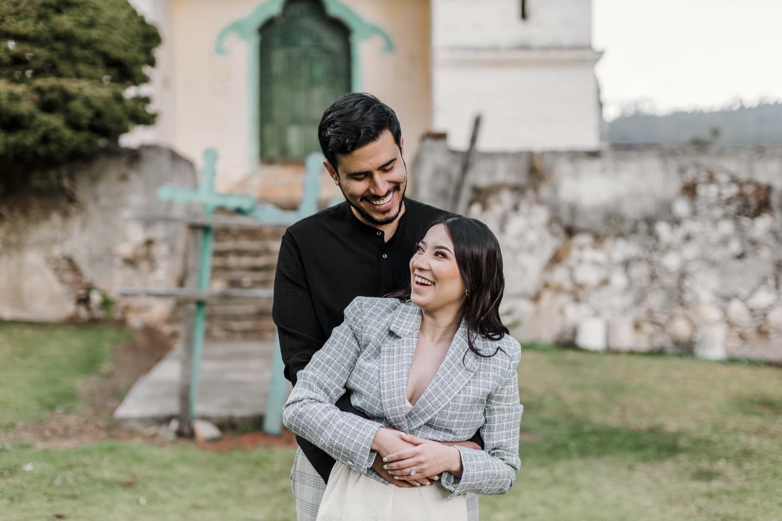 Andrea y Andrés abrazados, riéndose, en el atrio de una capilla.